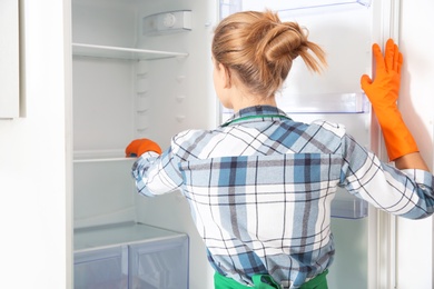 Woman in rubber gloves cleaning empty refrigerator at home