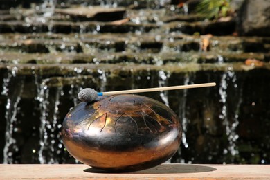 Steel tongue drum with mallet near waterfall outdoors on sunny day. Percussion musical instrument