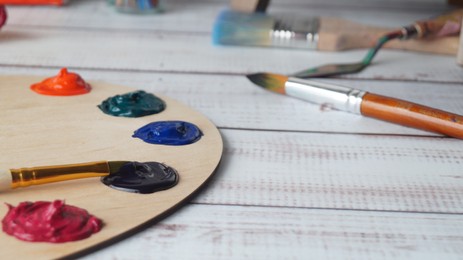 Photo of Artist's palette with samples of colorful paints and brushes on white wooden table, closeup