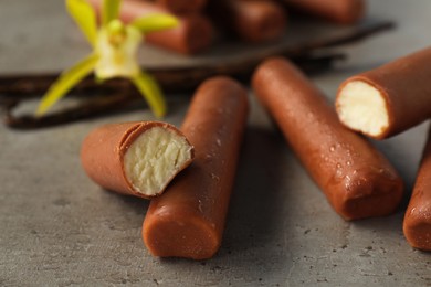 Photo of Glazed curd cheese bars, vanilla pods and flower on grey table, closeup