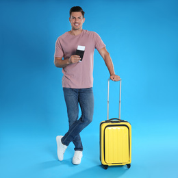 Photo of Man with suitcase and ticket in passport for summer trip on blue background. Vacation travel