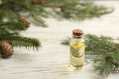 Glass bottle of essential oil and fir branches with cones on white wooden table