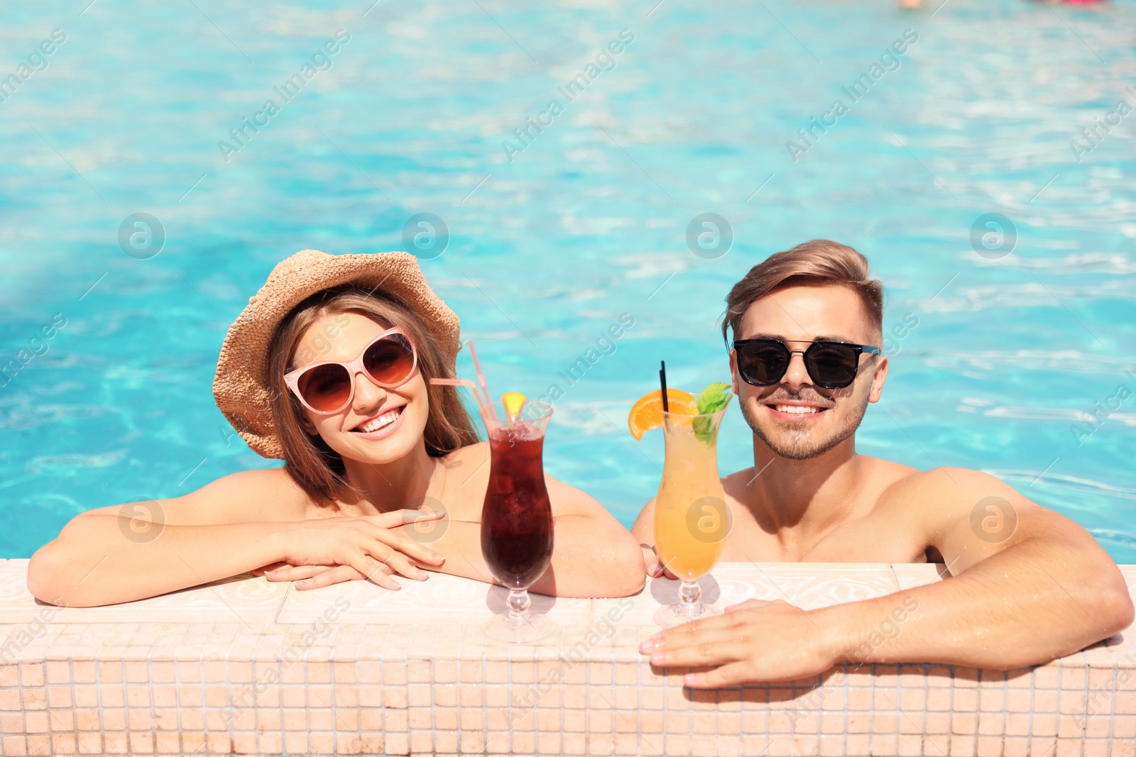 Photo of Young couple with cocktails in pool on sunny day