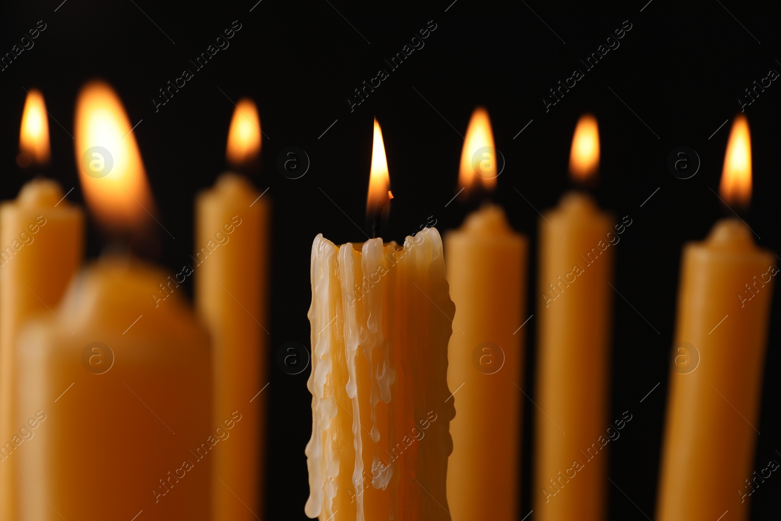 Photo of Many burning church candles on black background, closeup