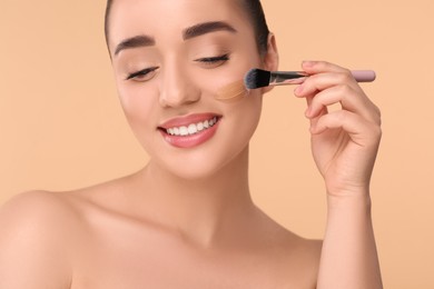 Photo of Woman applying foundation on face with brush against beige background