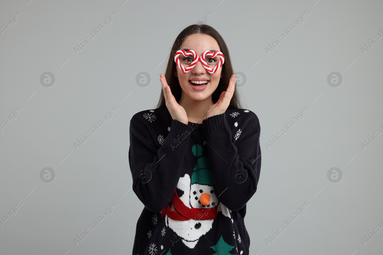 Photo of Happy young woman in Christmas sweater and funny glasses on grey background