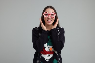 Photo of Happy young woman in Christmas sweater and funny glasses on grey background