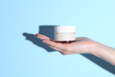 Woman holding jar of cream on light blue background, closeup