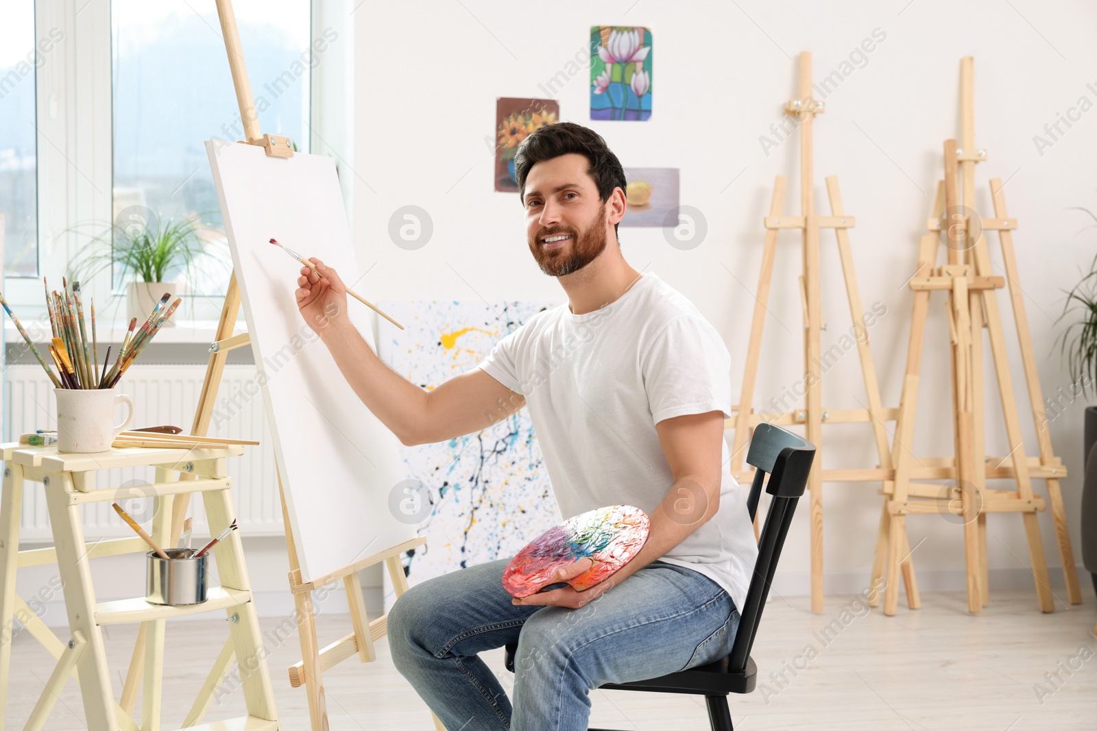 Photo of Happy man painting in studio. Using easel to hold canvas