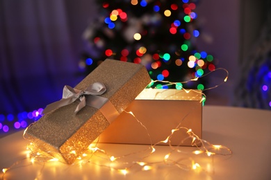 Photo of Gift box with fairy lights and blurred Christmas tree on background