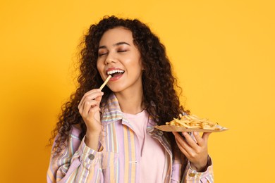 African American woman eating French fries on yellow background