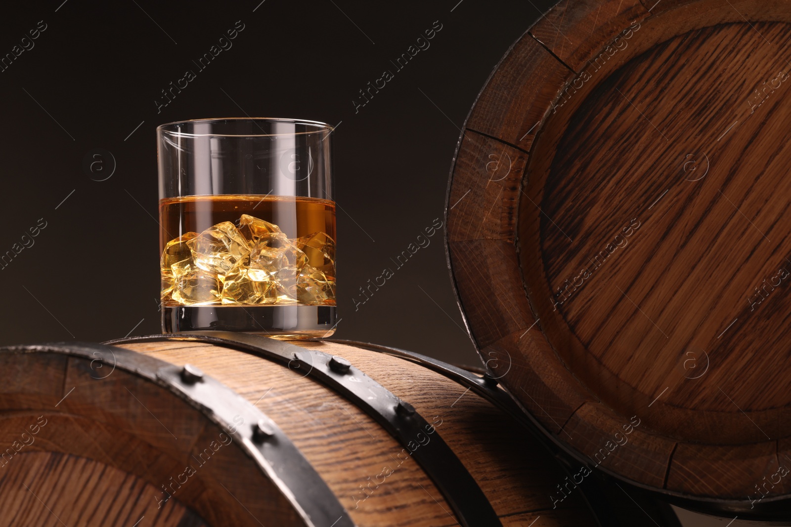 Photo of Whiskey with ice cubes in glass on wooden barrel against dark background