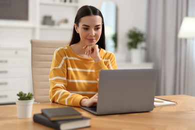 Photo of Young woman watching webinar at table in room