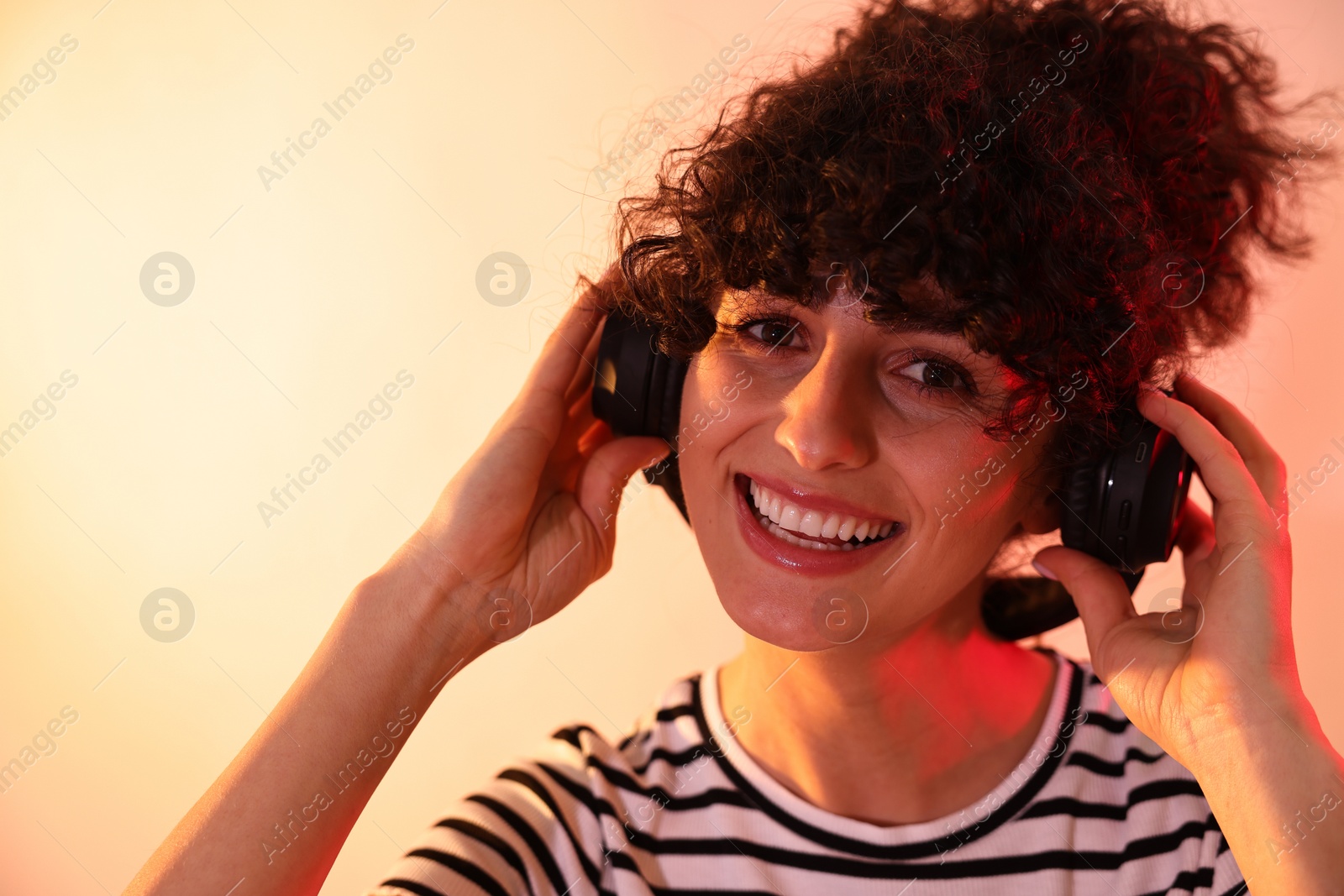 Photo of Beautiful young woman listening to music with headphones on color background in neon lights, closeup. Space for text