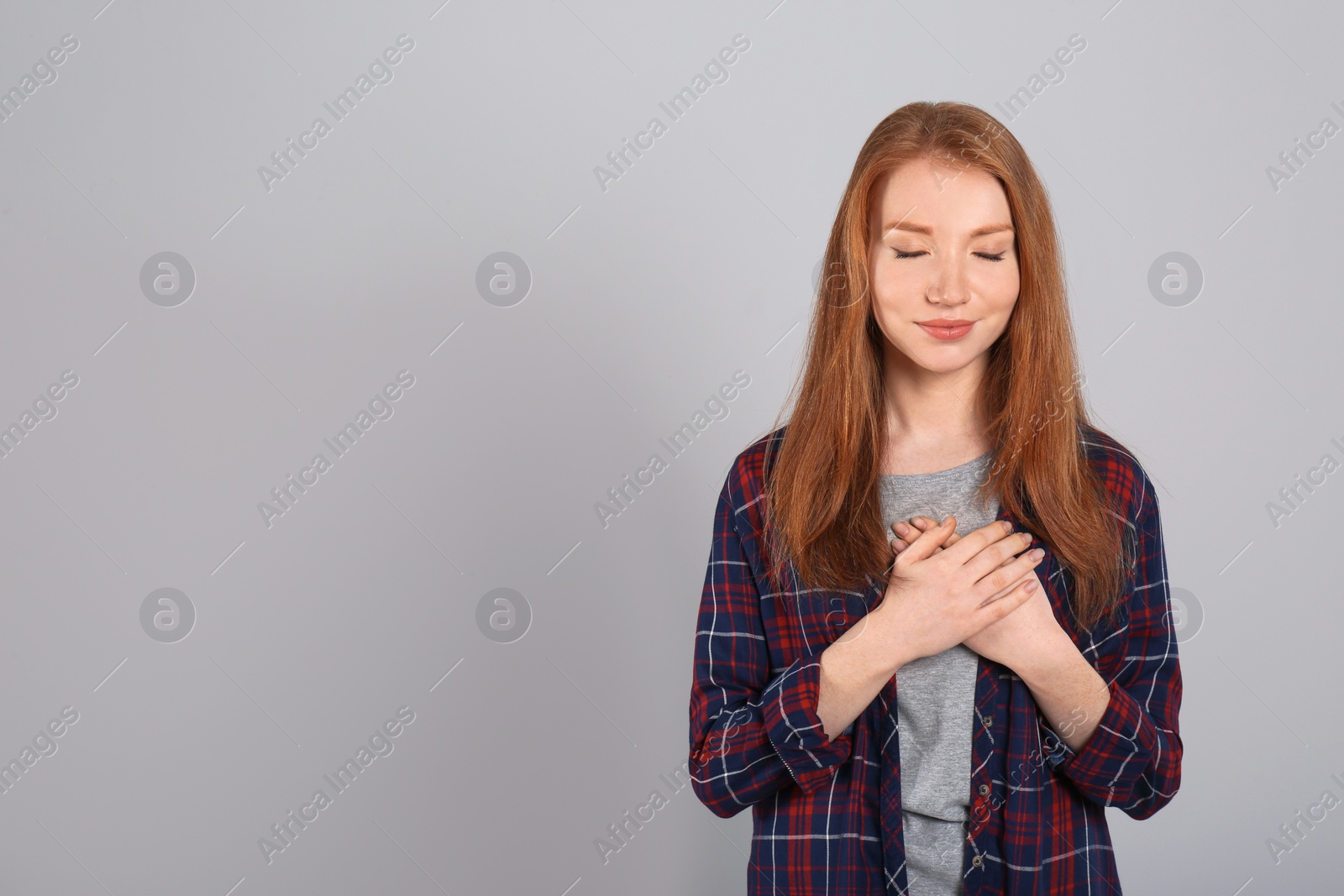 Photo of Beautiful grateful woman with hands on chest against light grey background. Space for text