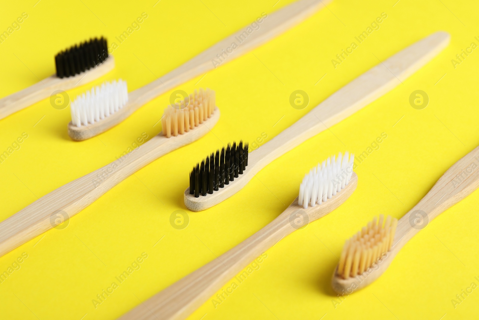 Photo of Bamboo toothbrushes on yellow background, closeup view