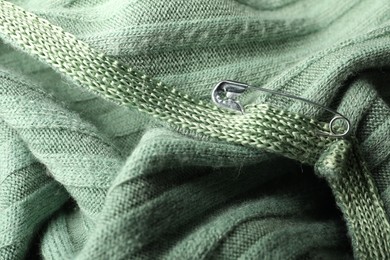 Photo of Metal safety pin on light green fabric, closeup