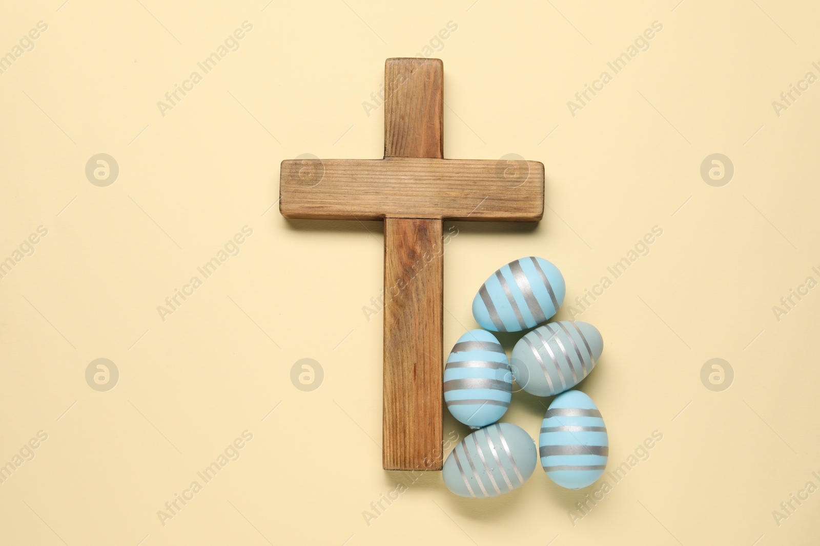 Photo of Wooden cross and painted Easter eggs on beige background, flat lay