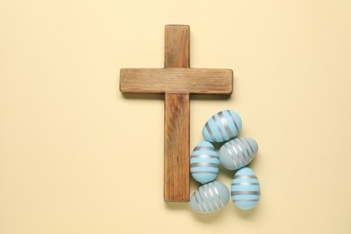 Photo of Wooden cross and painted Easter eggs on beige background, flat lay