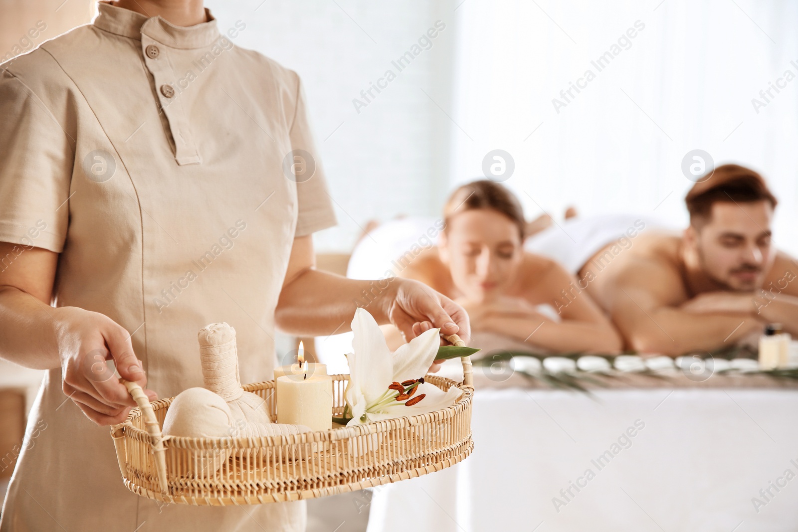 Photo of Massage therapist with spa essentials and young couple in wellness center