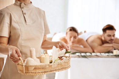 Massage therapist with spa essentials and young couple in wellness center