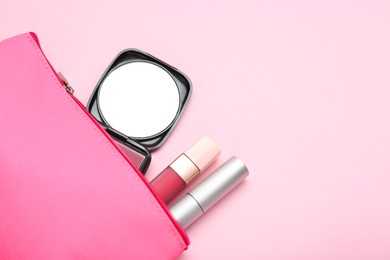Photo of Cosmetic bag with pocket mirror and makeup products on pink background, flat lay. Space for text