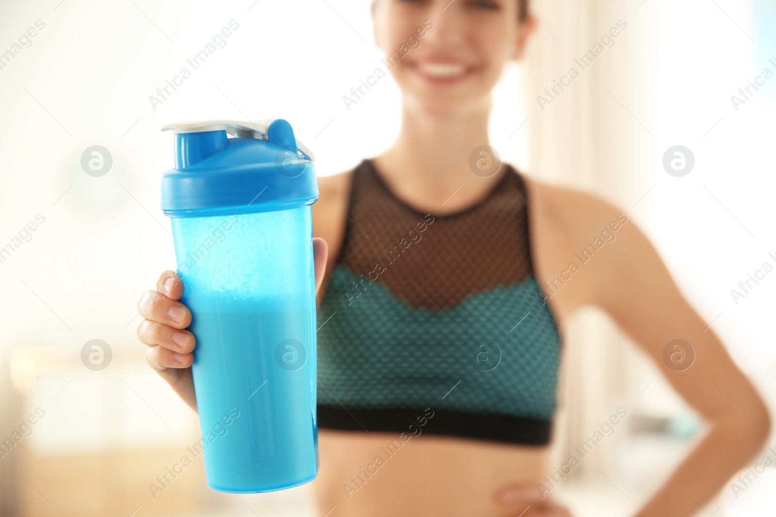 Photo of Young sporty woman with bottle of protein shake at home, closeup