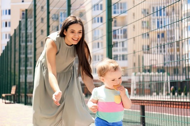 Photo of Woman supporting her baby daughter while she learning to walk outdoors