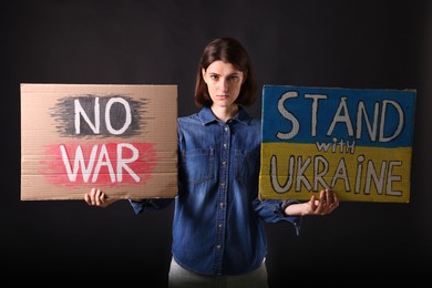 Sad woman holding posters with phrases NO WAR and Stand with Ukraine on black background