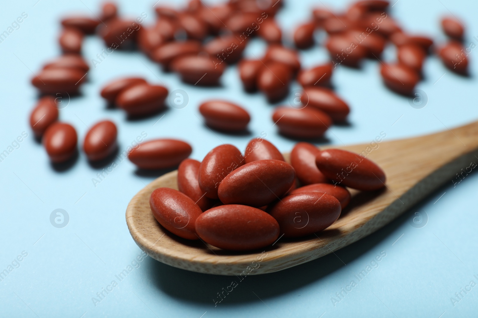 Photo of Wooden spoon with pills on light blue background, closeup