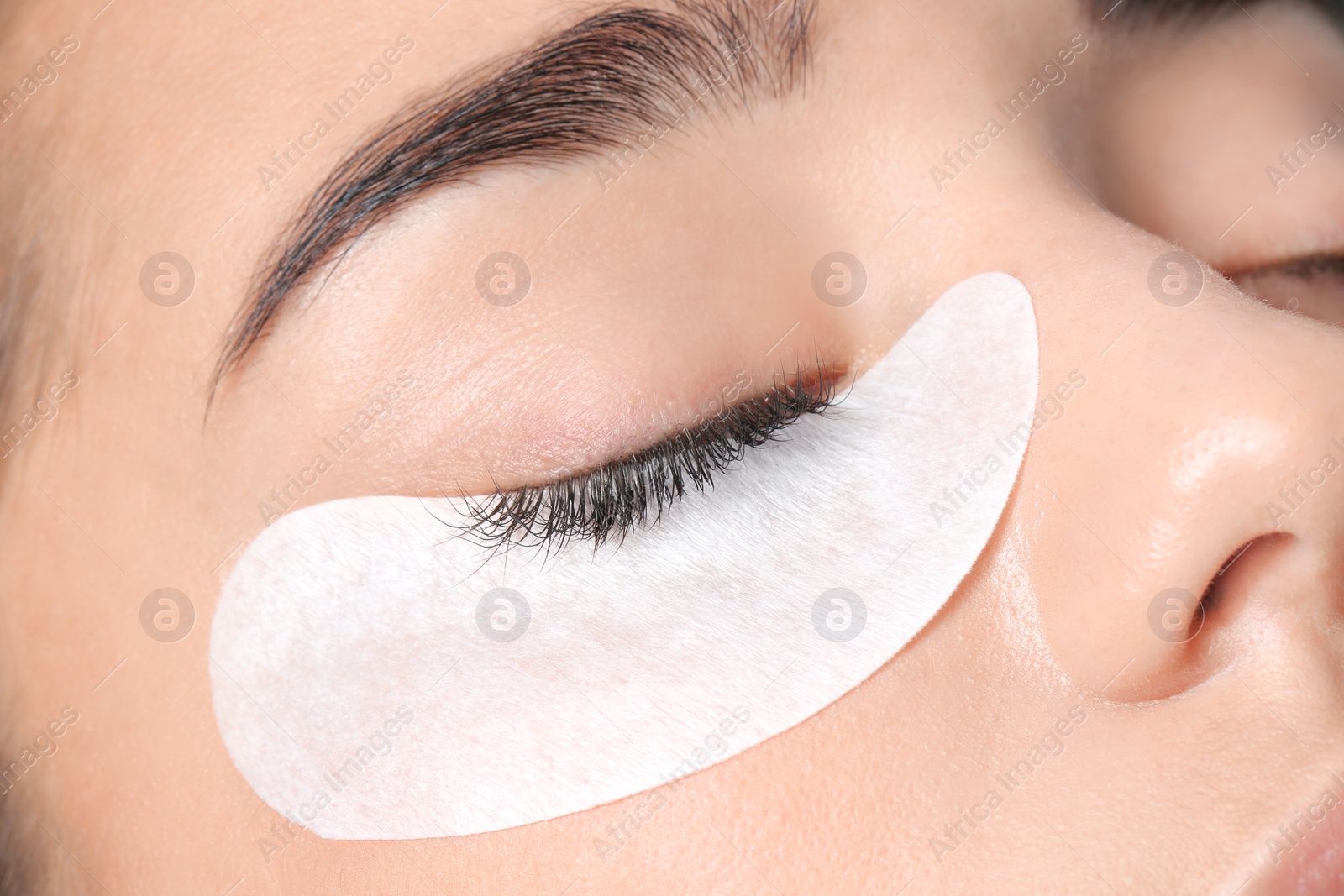 Photo of Young woman undergoing eyelashes extensions procedure, closeup