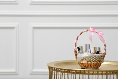 Photo of Gift set in wicker basket on golden table near white wall. Space for text