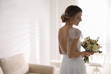 Gorgeous bride in beautiful wedding dress holding bouquet in room. Space for text