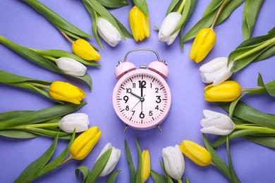 Pink alarm clock and beautiful tulips on violet background, flat lay. Spring time