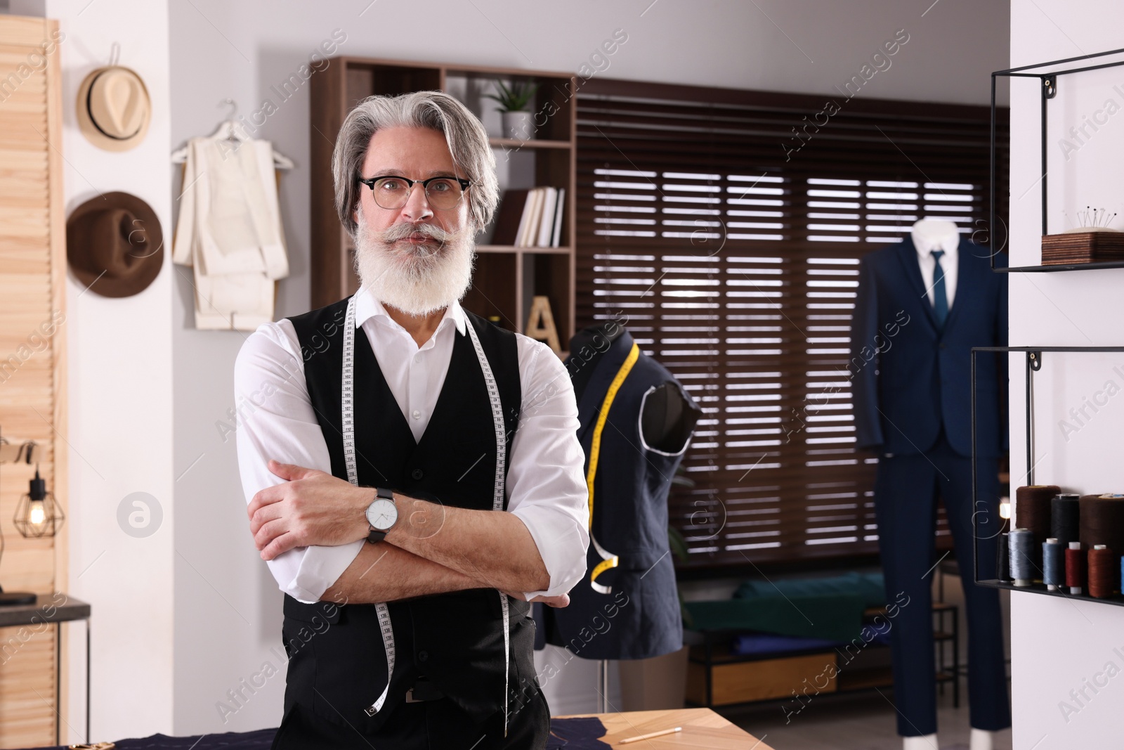 Photo of Professional tailor with measuring tape in workshop, space for text