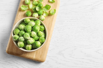 Board with bowl and Brussels sprouts on wooden background, top view. Space for text