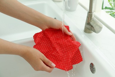 Photo of Woman washing beeswax food wrap under tap water in kitchen sink, closeup