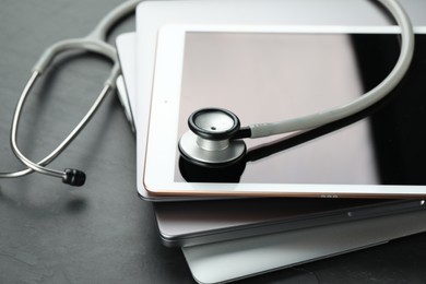 Stack of electronic devices and stethoscope on black table, closeup