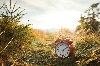 Red alarm clock on grass outdoors in morning, space for text