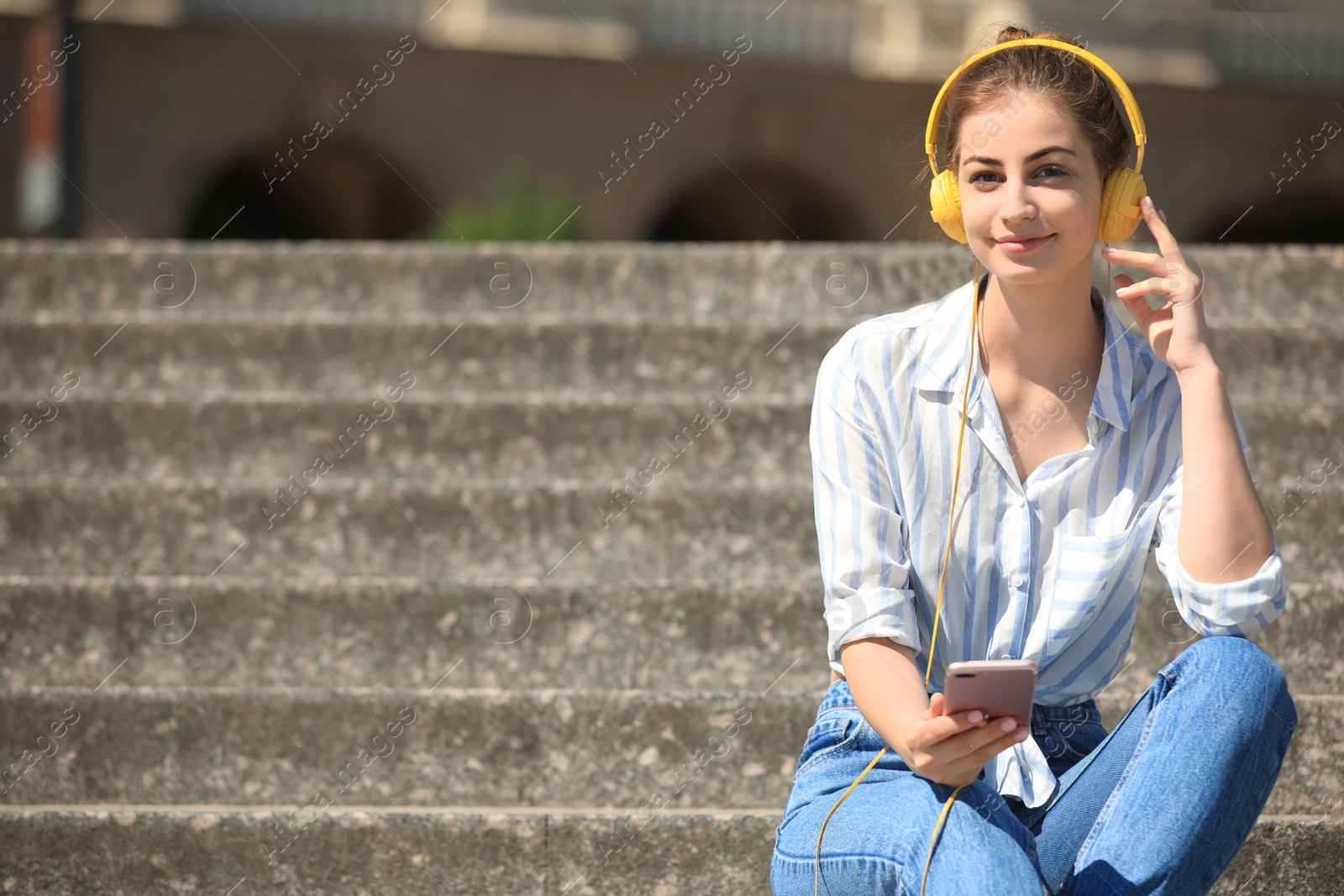 Photo of Young woman with headphones listening to music on stairs. Space for text