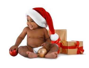 Cute African-American baby wearing Santa hat with Christmas gifts on white background