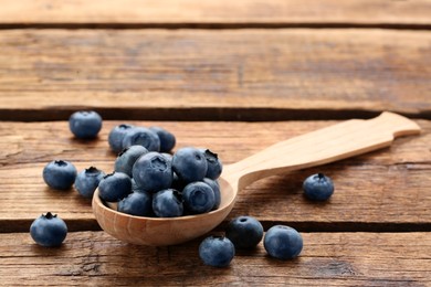 Photo of Spoon with tasty fresh blueberries on wooden table