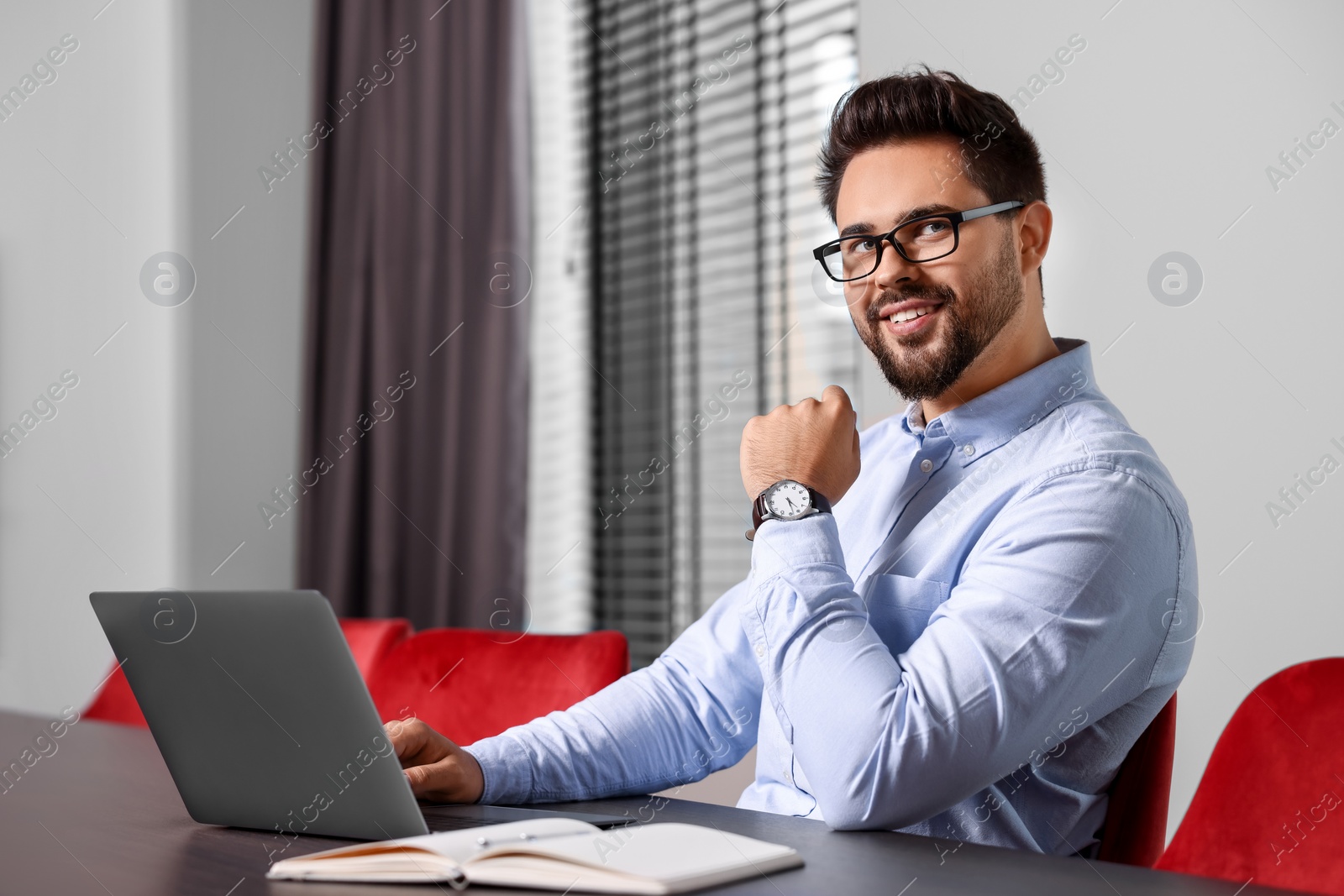 Photo of Happy young man working on laptop at table in office