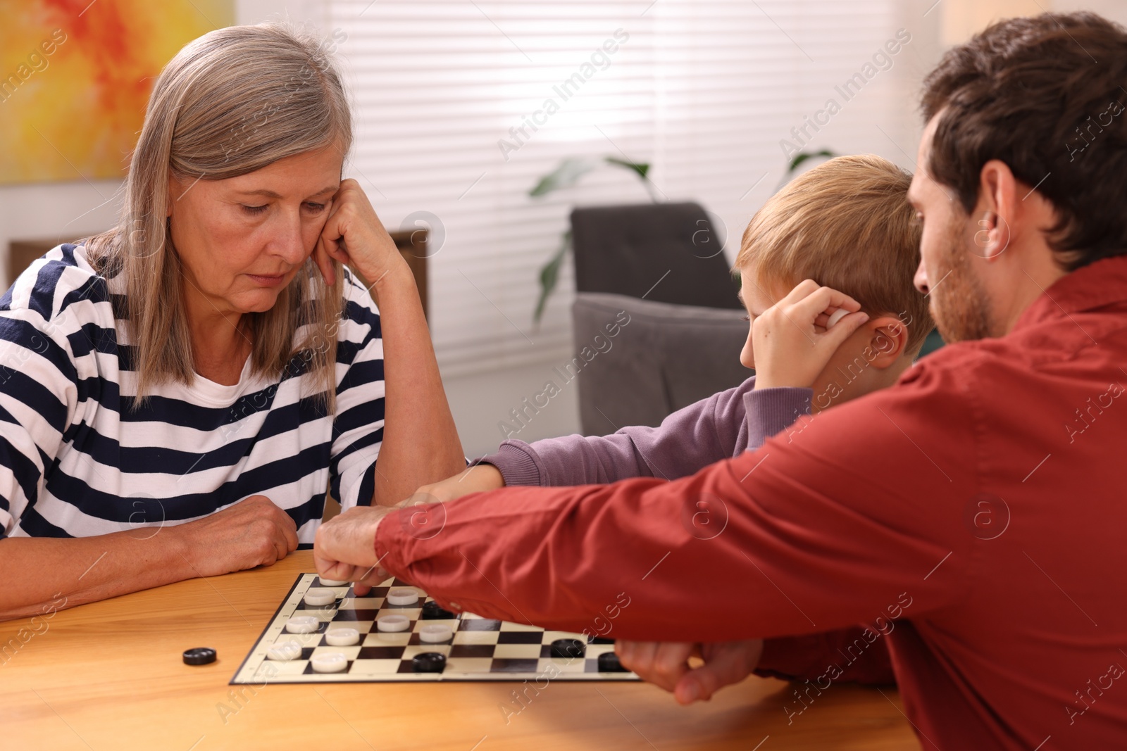 Photo of Family playing checkers at wooden table in room