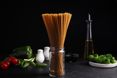 Photo of Uncooked buckwheat noodles and fresh ingredients on black table