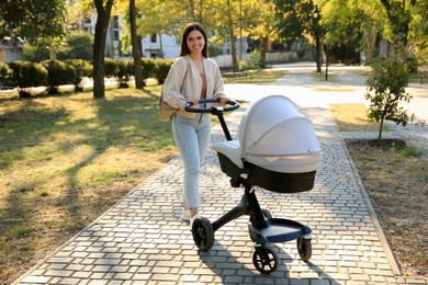 Photo of Young mother walking with her baby in stroller at park on sunny day