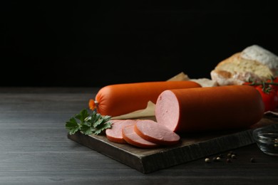 Photo of Board with tasty boiled sausages on dark wooden table against black background. Space for text