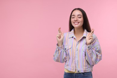 Photo of Happy woman crossing her fingers on pink background, space for text