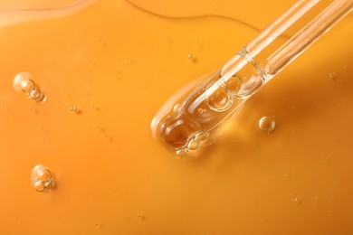 Photo of Dripping hydrophilic oil from pipette on orange background, closeup