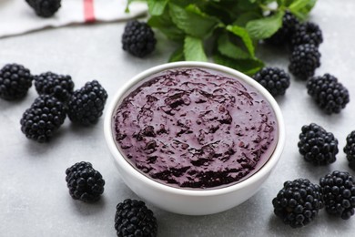 Photo of Blackberry puree in bowl and fresh berries on light grey table, closeup